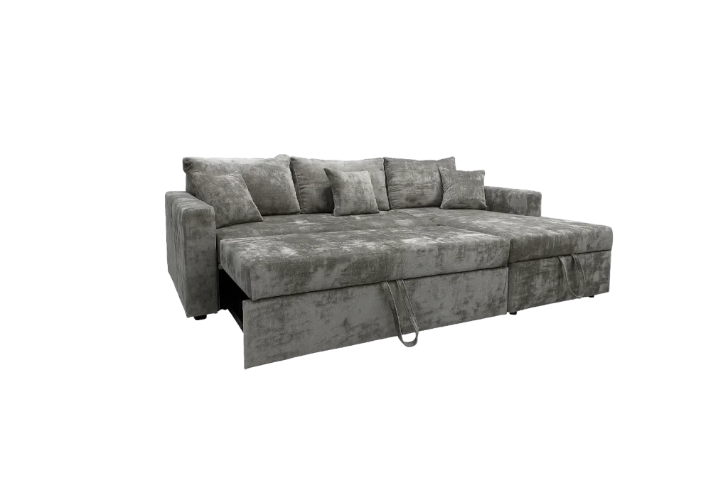 L-shaped grey velvet sofa cum bed with decorative pillows, a footrest, and a pull-out bed for versatile seating and sleeping options.