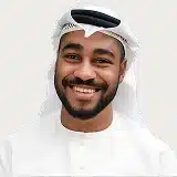 A smiling man with a beard wearing a white shirt, exuding a friendly and approachable demeanor.